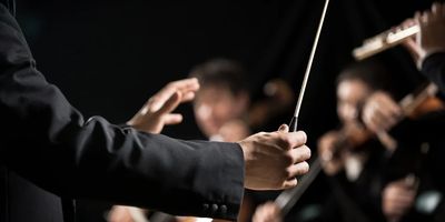 Closeup picture of an orchestra conductor holding a baton.