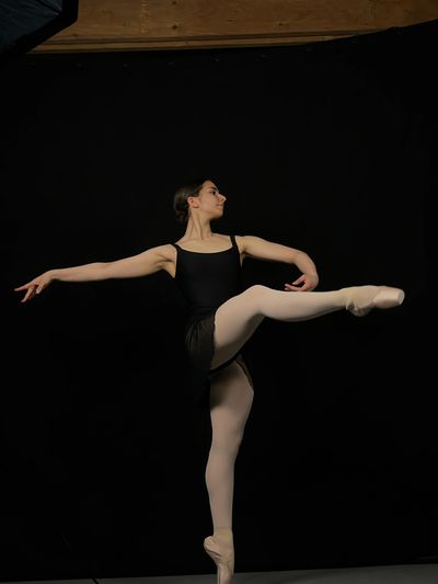 Ballet dancer in black leotard and pink tights performing an elegant pose.