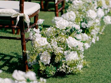 Elegant white silk flower wedding rentals aisle markers by wooden chairs at Fete the Venue in Costa Mesa.