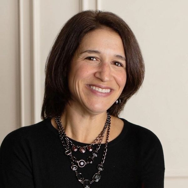 A picture of Laura Cantagallo ink a black shirt with a necklace on and an off white background.