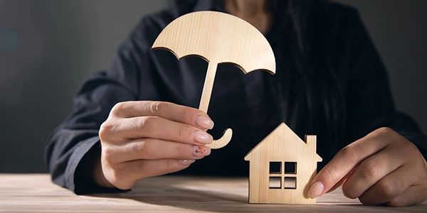 une personne tenant un parapluie d'une main et de l'autre une maison, assurance habitation