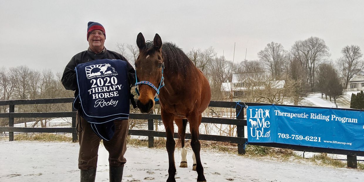 Man with horse holding a 2020 Therapy Horse award blanket outdoors in winter.