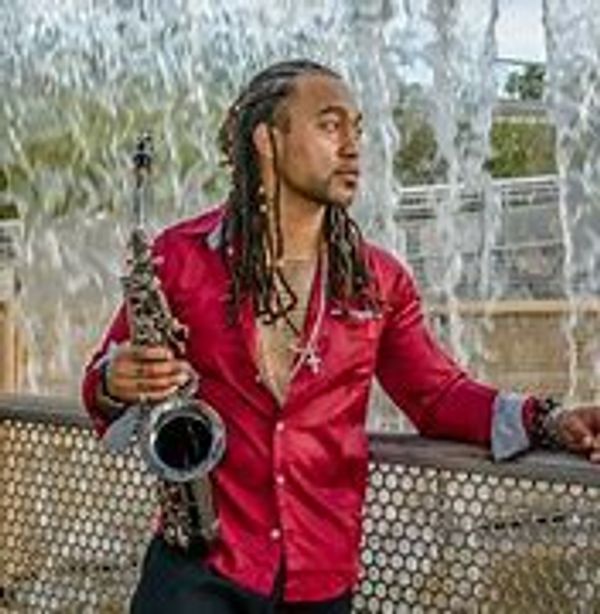 Man in red shirt holding saxophone near a waterfall.