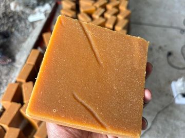 Hand holding a square block of jaggery with more blocks in the background.