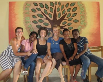 Group of six diverse women sitting and smiling in front of a colorful tree mural.
