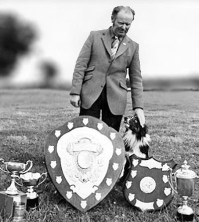 Man with dog and trophies on grass field.
