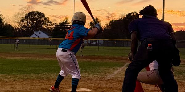 A young baseball player at bat during a sunset game.