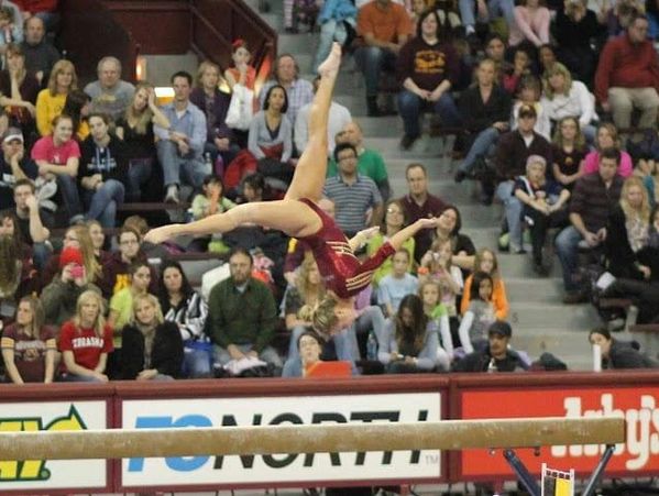 Gymnast performing a backflip on the balance beam in front of a crowd.