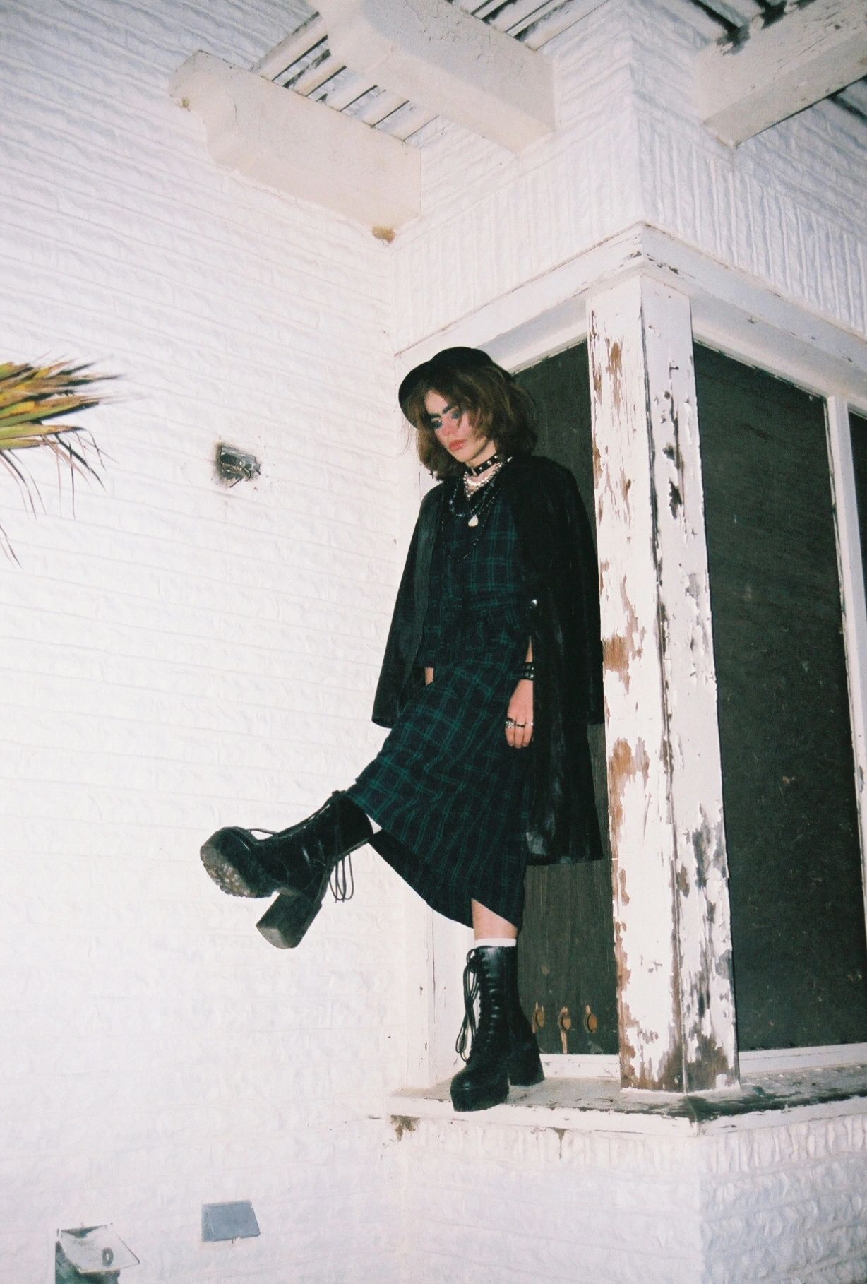 Person in dark fashion outfit posing against a white brick wall.