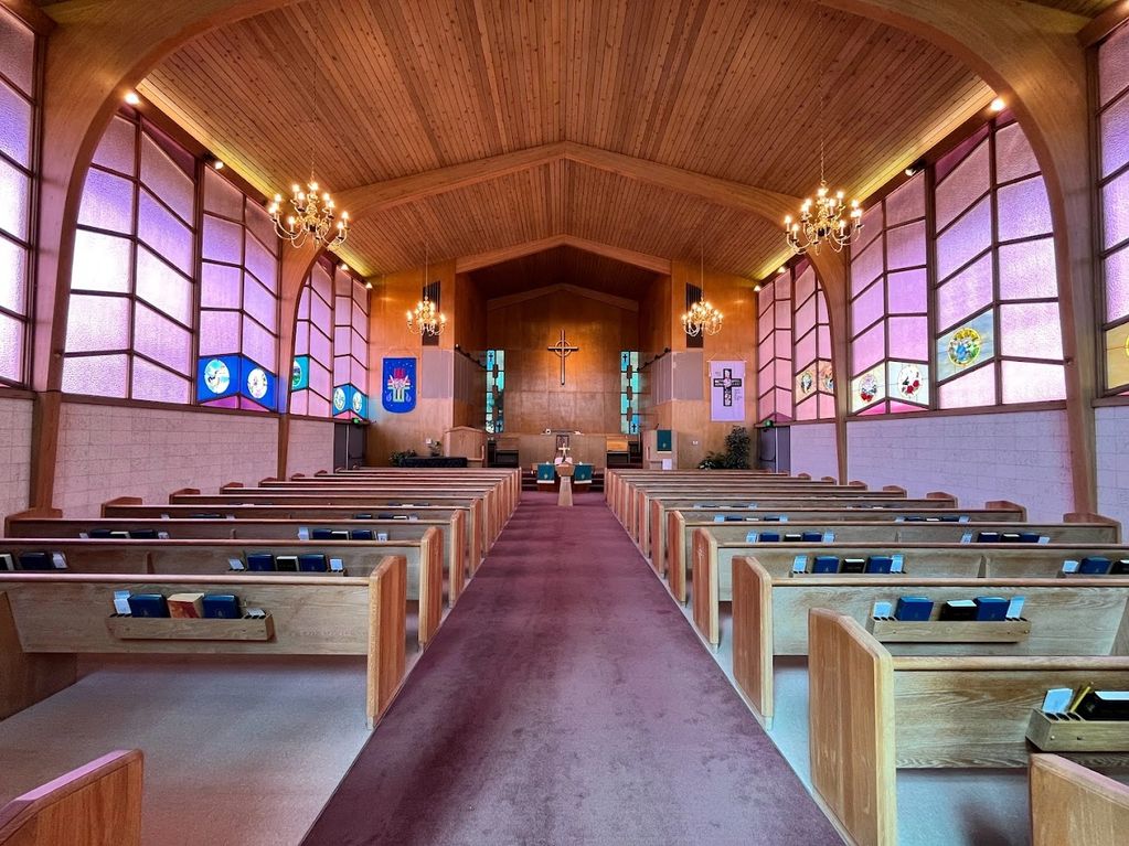 Interior of a wooden church with purple stained glass and chandeliers.