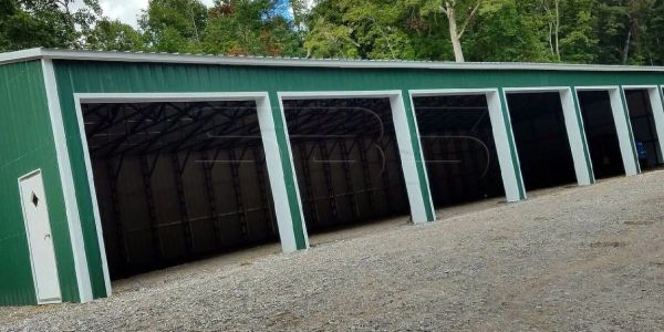 Green storage building with multiple open garage doors.