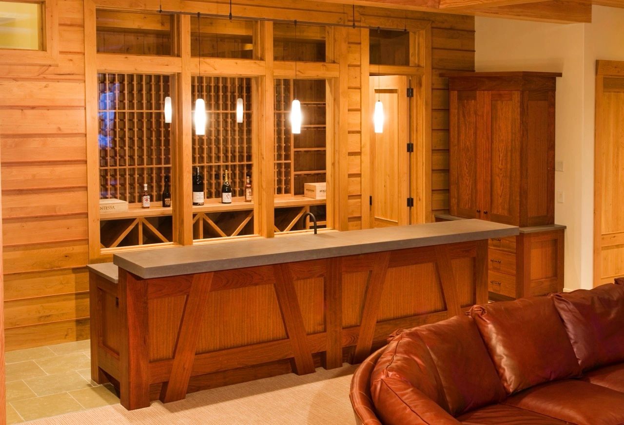 This bar has rich wooden accents, a sleek concrete countertop, a wooden wine rack, pendant lights