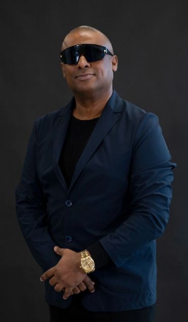Man in dark blazer and sunglasses with gold watch.