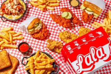 A spread of crispy fried chicken, crinkle-cut fries, and dipping sauces on a checkered tablecloth.