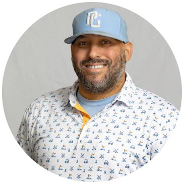 Smiling man in a blue cap and patterned shirt.