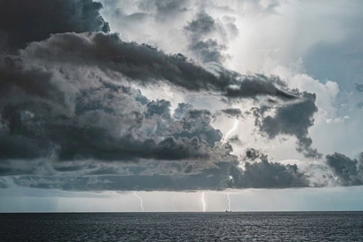 Dark storm clouds over ocean with lightning strikes on the horizon.