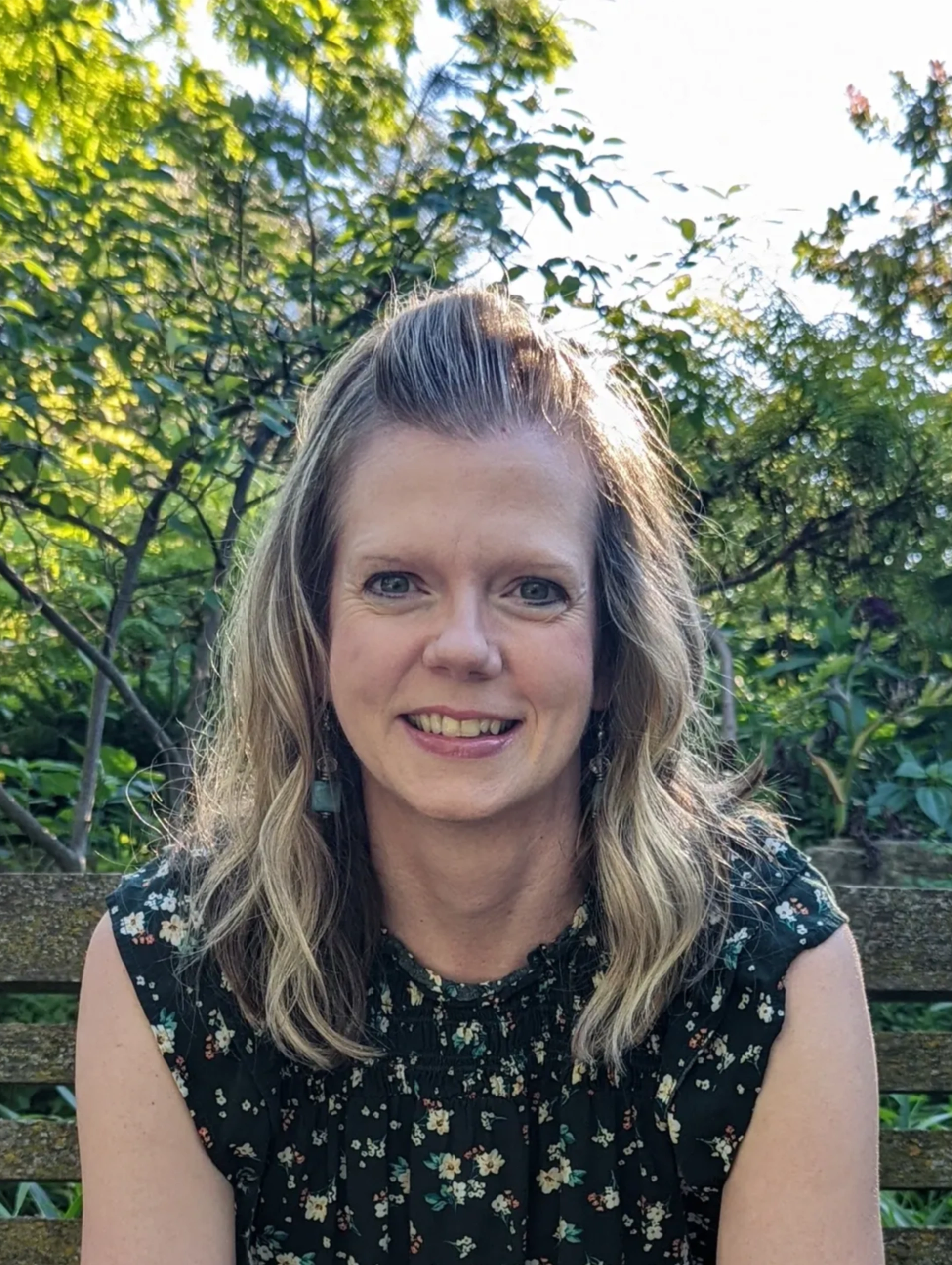 Woman sitting on a wooden bench in a lush garden, smiling.