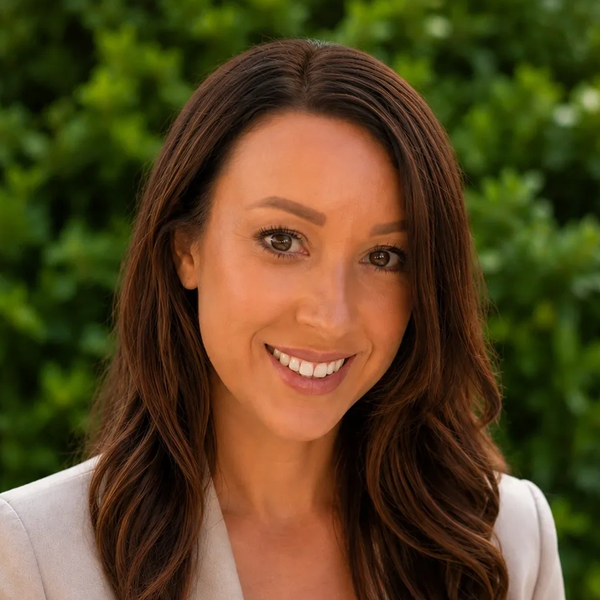 Smiling woman with long brown hair in front of greenery.