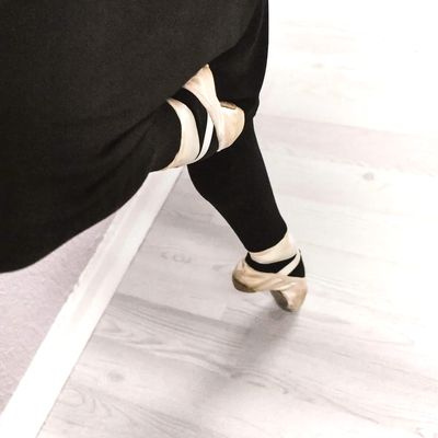 ballet dancer's feet in pointe shoes with one foot en pointe and the other foot lifted to the knee