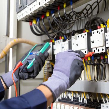 Electrician in gloves testing electrical panel connections with a multimeter.