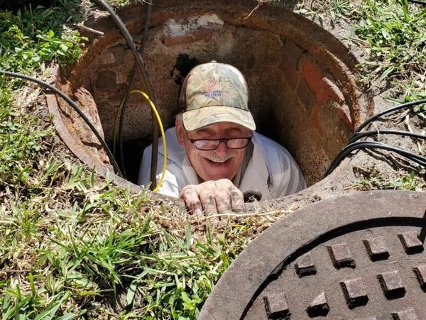 A photo of a plumber smiling and climbing out of a sewer manhole.