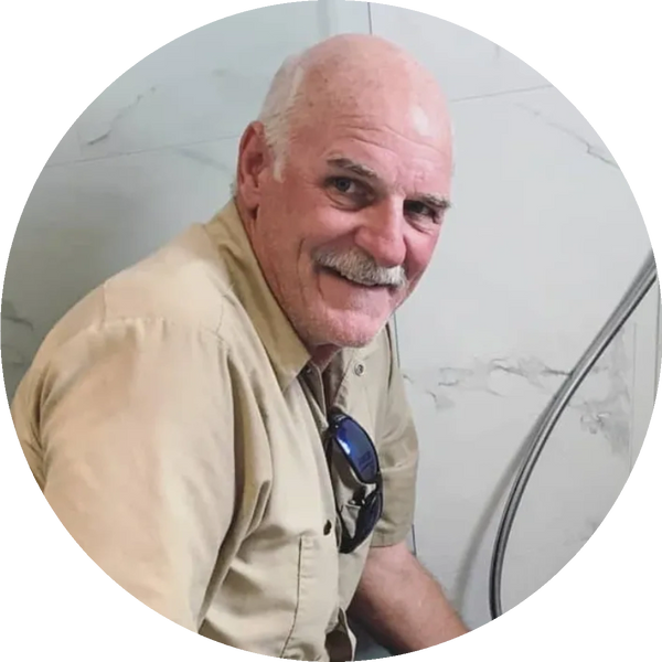 A photo of a plumber pausing to smile while working in a marble shower stall.