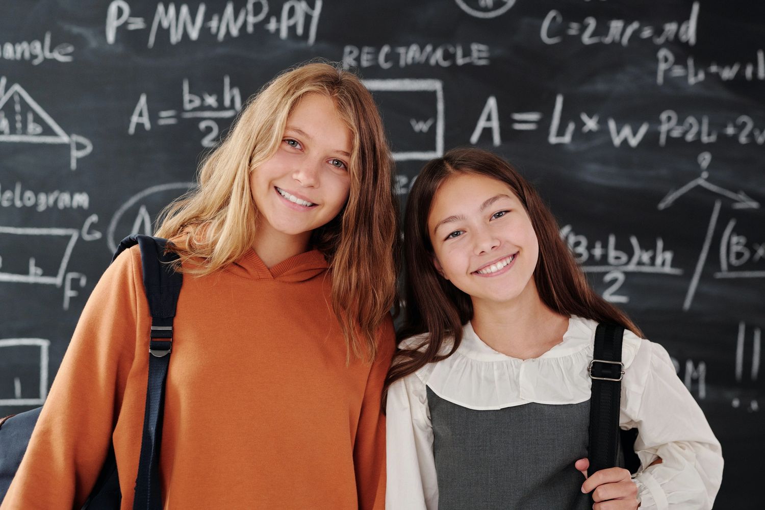 two girls standing in front of a blackboard with math equations smiling