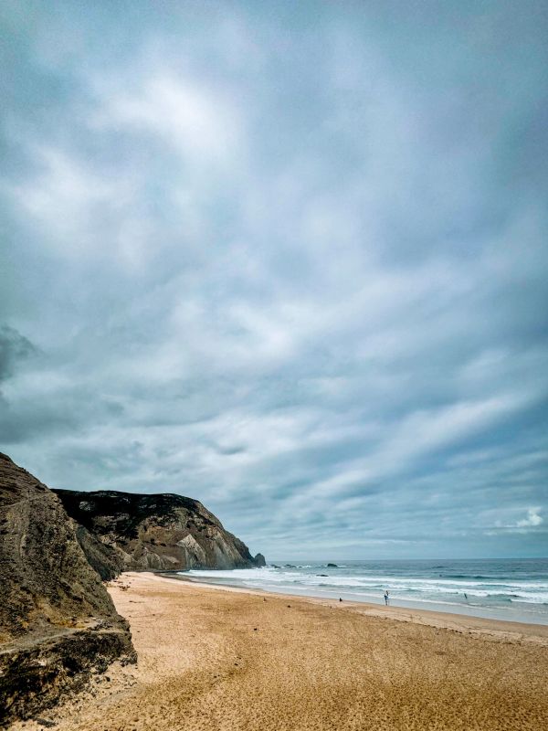Strand mit Felsen und bewölktem Himmel.
