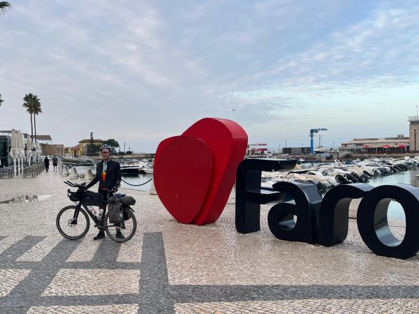 Person mit Fahrrad vor Faro-Skulptur am Hafen.