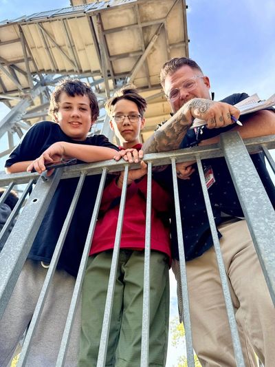 Three people leaning on a metal railing under a structure, smiling at the camera.