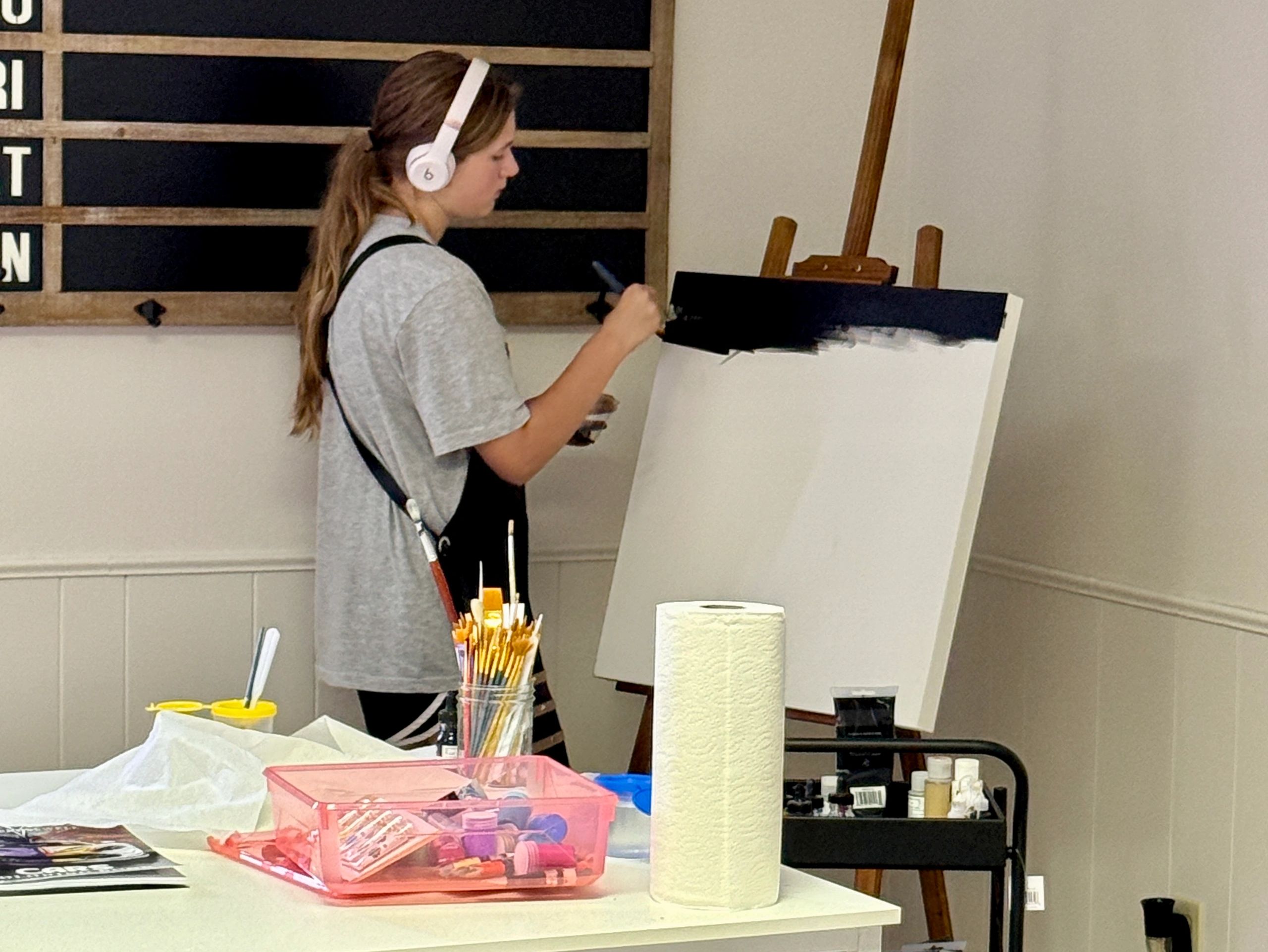 Young woman painting on a canvas with headphones on.