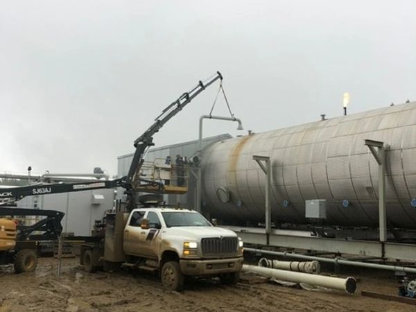 Work truck with crane servicing large industrial tank in muddy area.