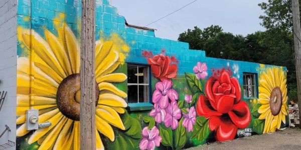 Colorful mural of sunflowers, roses, and pink flowers on a blue wall.
