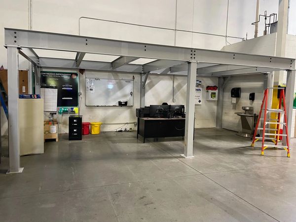 A steel mezzanine structure installed in a warehouse, with a desk, whiteboard, underneath.