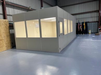 A new beige modular office with several windows, lights on inside an industrial setting by SoFlo Ins