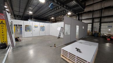 A modular office building under construction with light-colored wall panels, exposed metal ceiling f