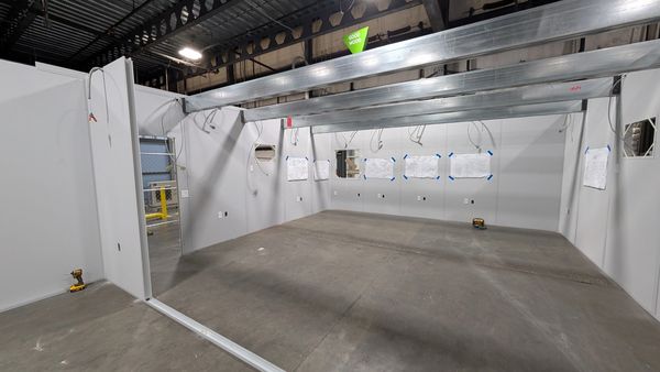 A modular installation building under construction, featuring light-colored wall panels, exposed 