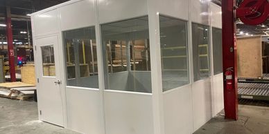 "A white modular office with large windows on three sides and a door on the front."
