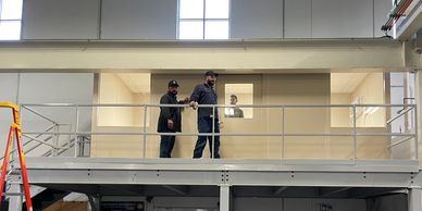 A group of men are working on the construction of a mezzanine level in a warehouse or industrial.