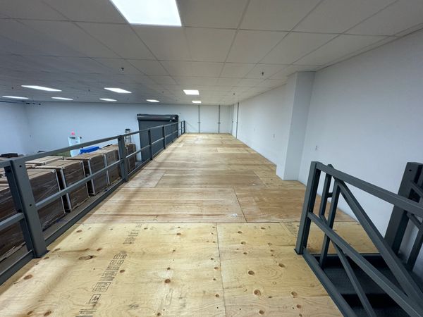 An empty mezzanine level in an industrial building. The mezzanine has a plywood floor, and railings.