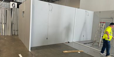 A worker is constructing a modular clean-room within a warehouse. 