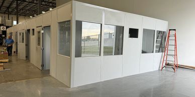 "A modular office with white walls and glass windows inside a warehouse."