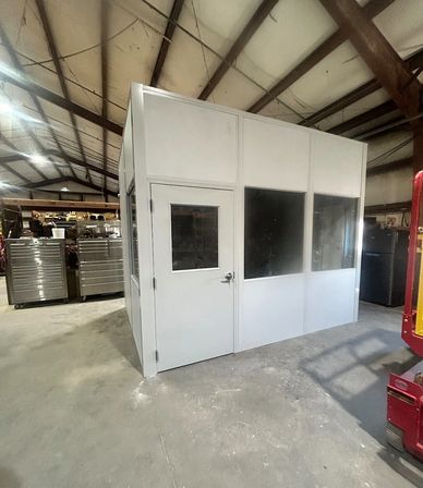 A modular grey office building installed inside an industrial warehouse, the building has windows & 