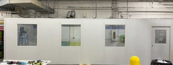 A newly constructed modular office installation with several windows and a door inside a warehouse 