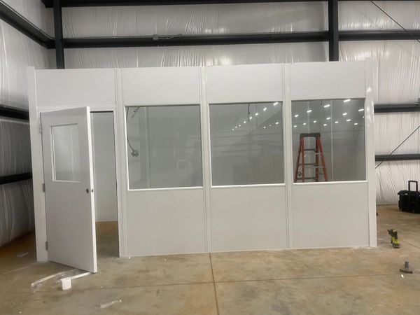 A prefabricated modular office with large glass windows and a door stands in a warehouse or industri