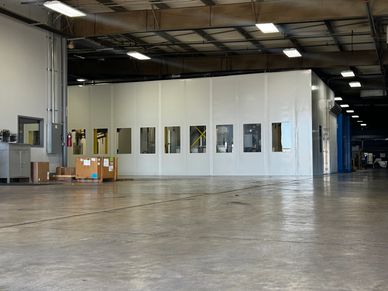 A large, white modular tool room inside a manufacturing facility. The room has several windows and a large door.
