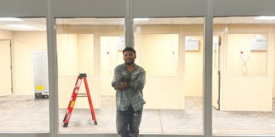 Me in a plaid shirt and jeans stands with his arms crossed, leaning against a glass partition.
