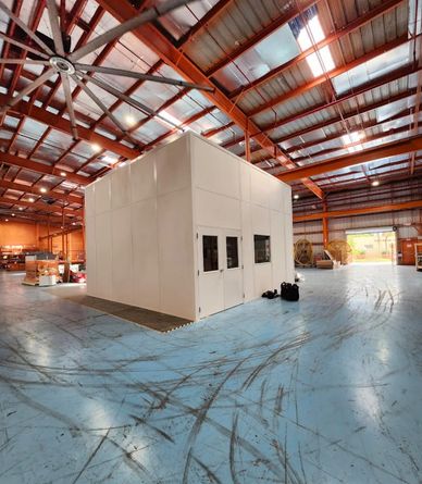 A large, white, modular structure stands in the middle of a warehouse. 