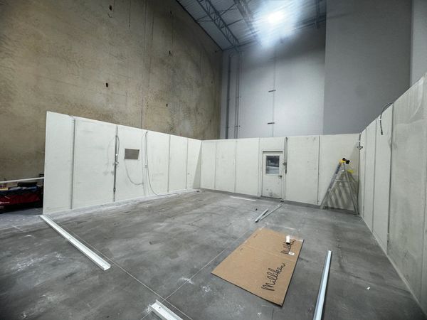 Three modular office walls being constructed inside a warehouse with a door & AC panel. Built by SoF