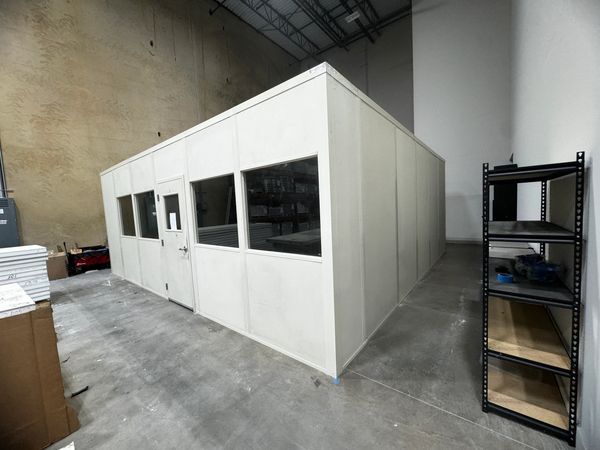 A light beige modular installation building in a corner with several windows, door in front. Built b